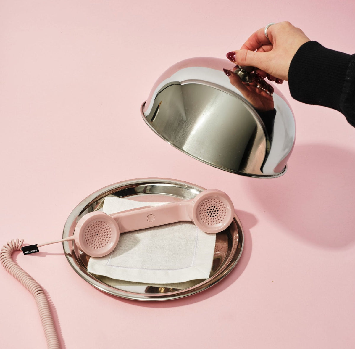 A pink telephone handset under a silver cloche